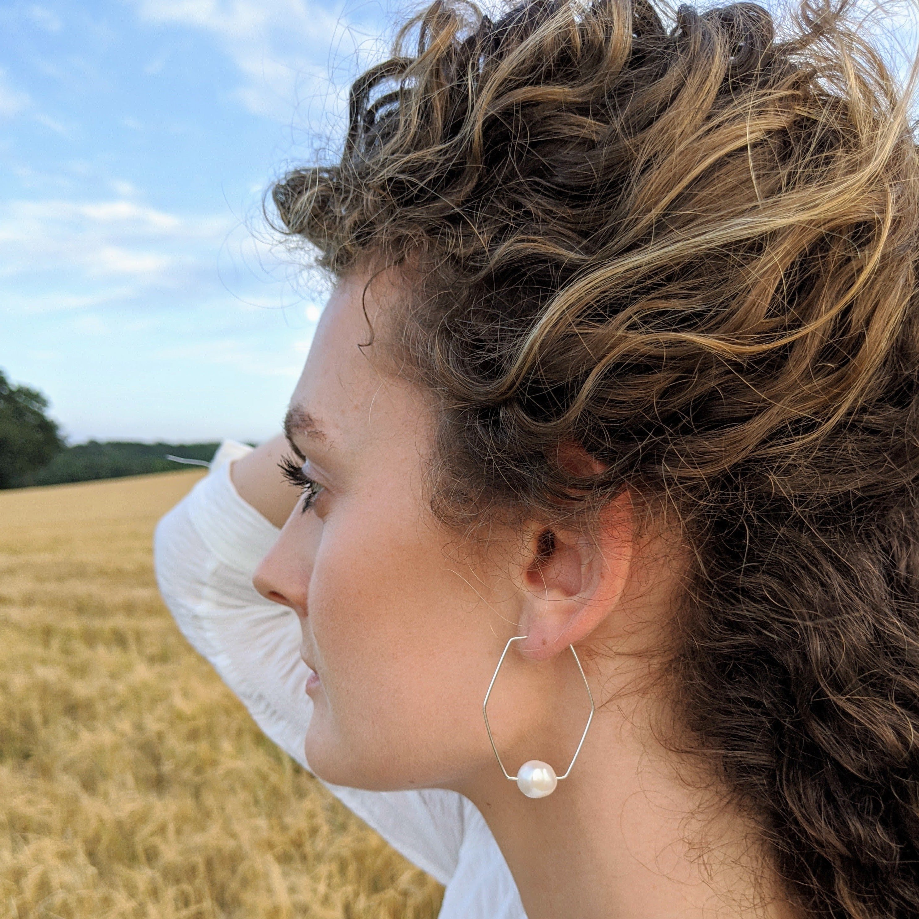 Large hexagonal geometric pearl hoop earrings on a model in a field