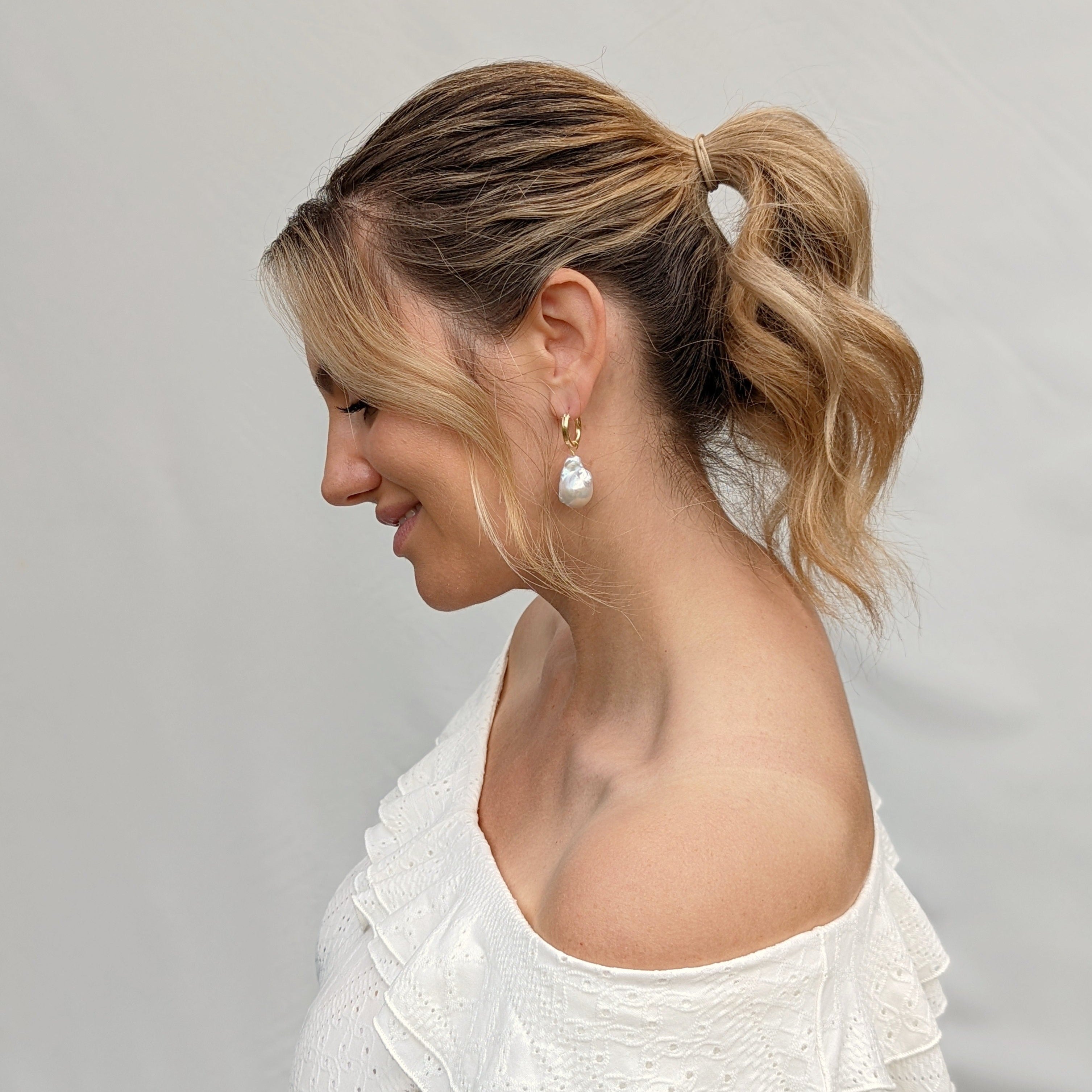 Model wearing white top and large fireball pearl earrings