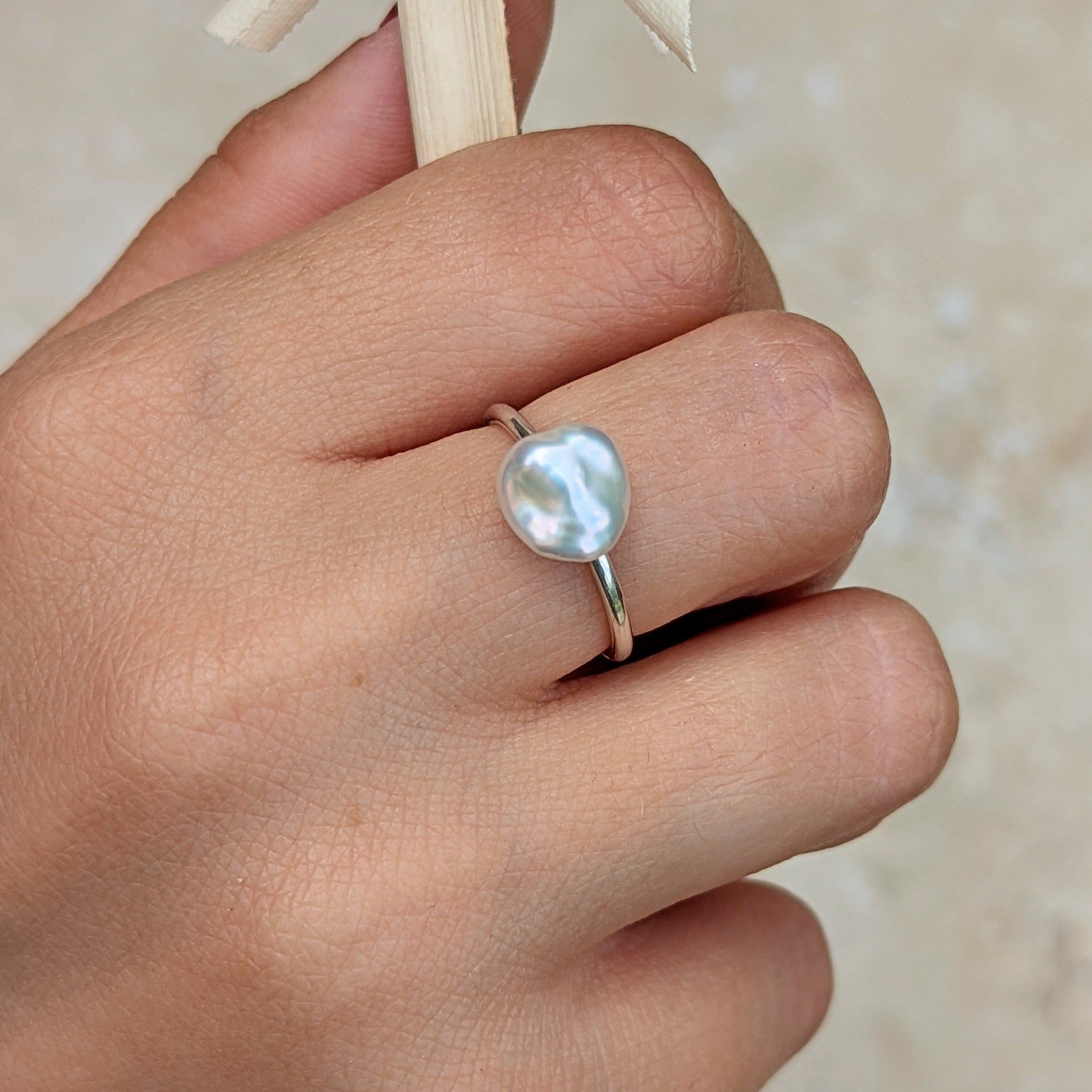 Hand holding dried branch wearing large baroque pearl ring with silver band