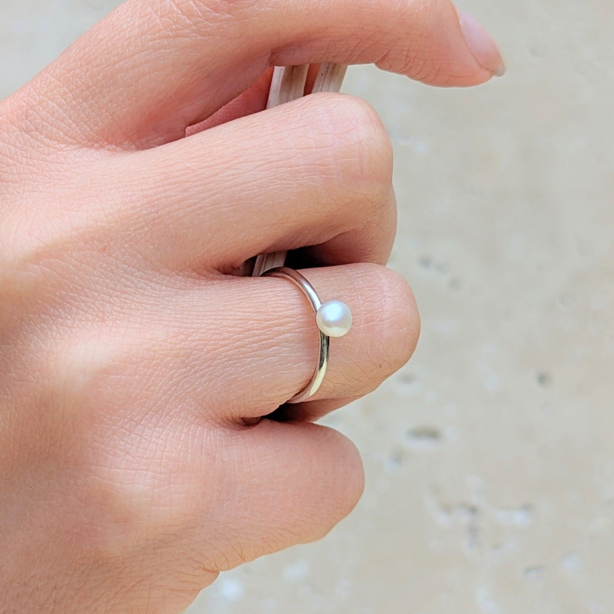 solitaire pearl ring in silver on hand holding branch