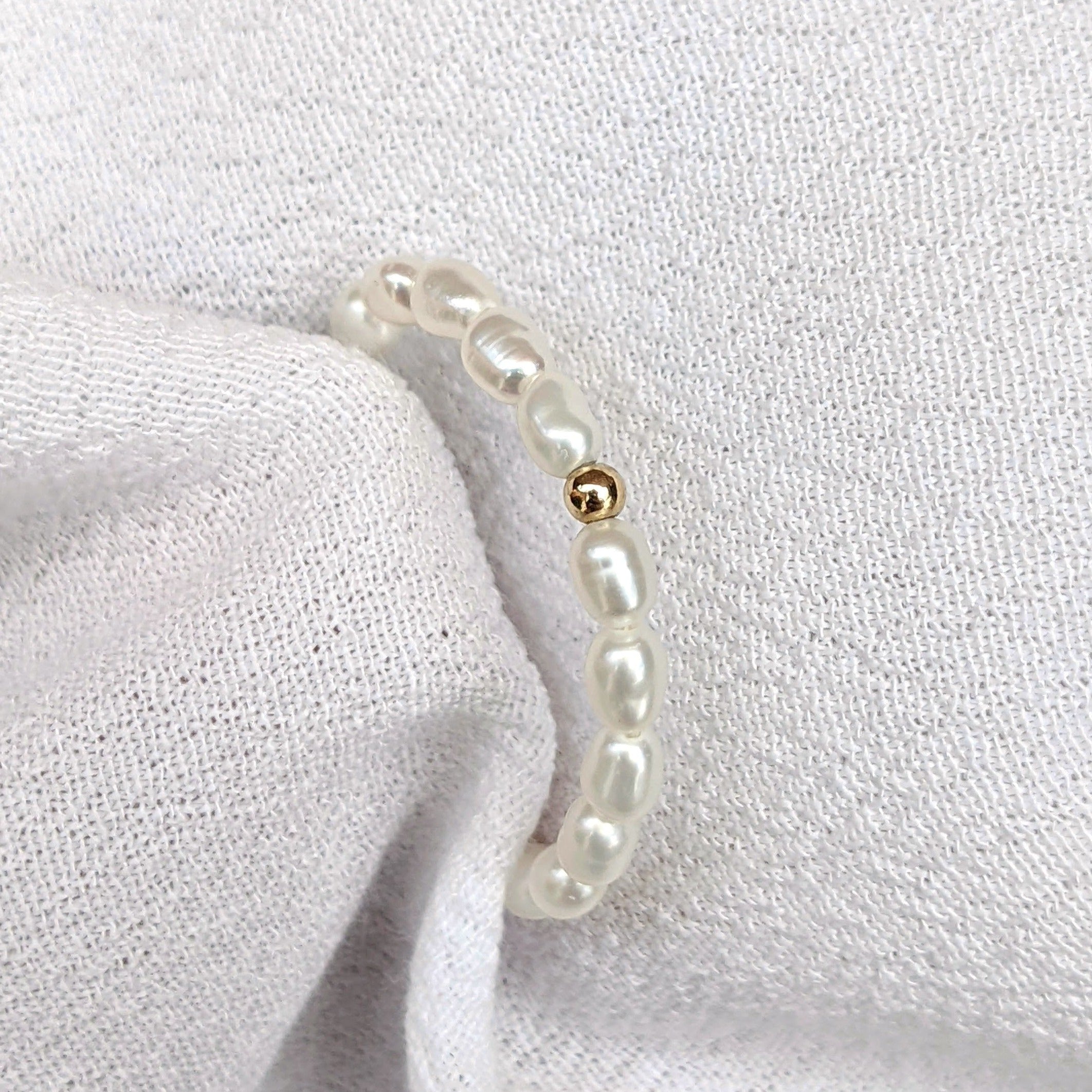 Single gold bead on pearl ring in white fabric