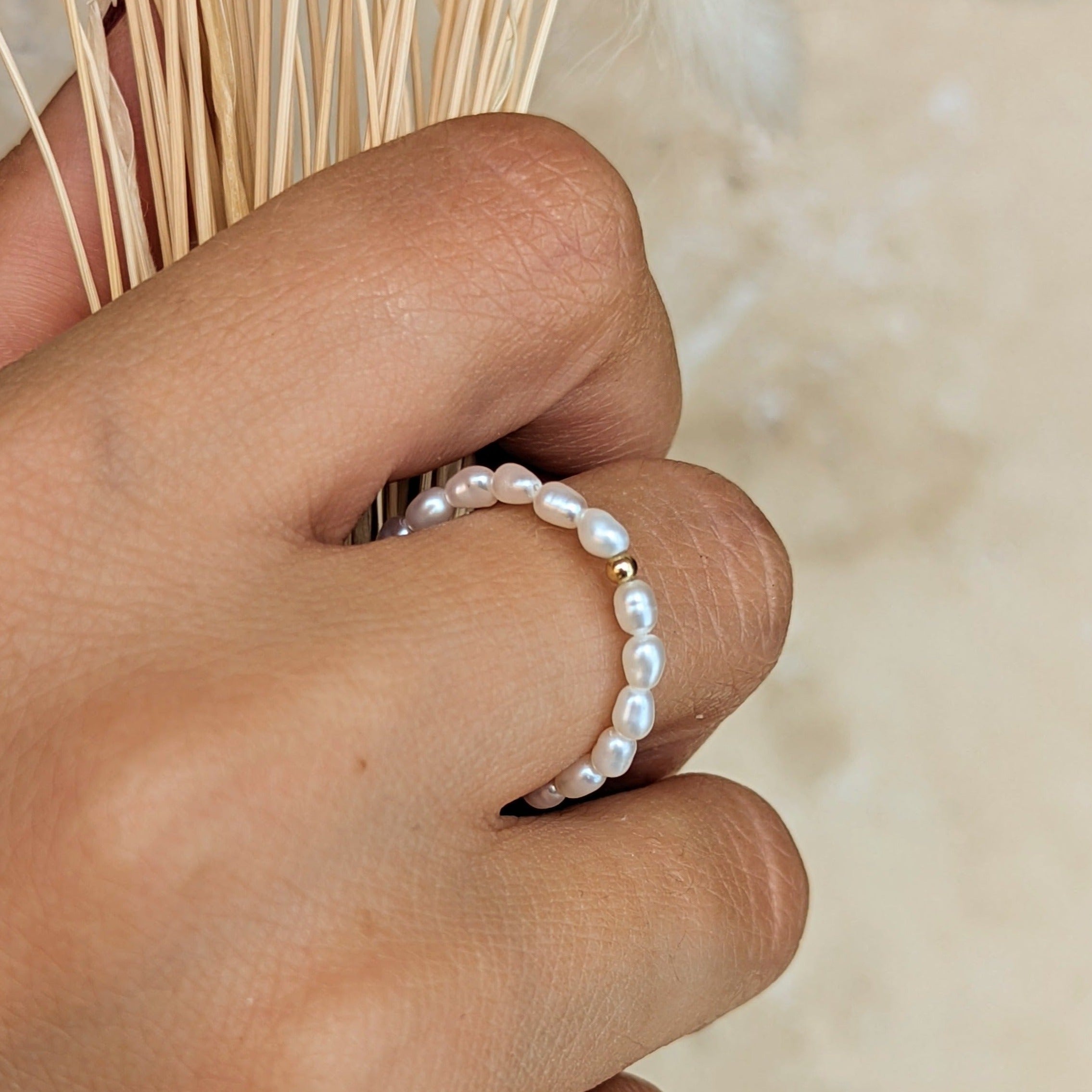 Hand holding dried grass wearing a pearl ring with small gold bead