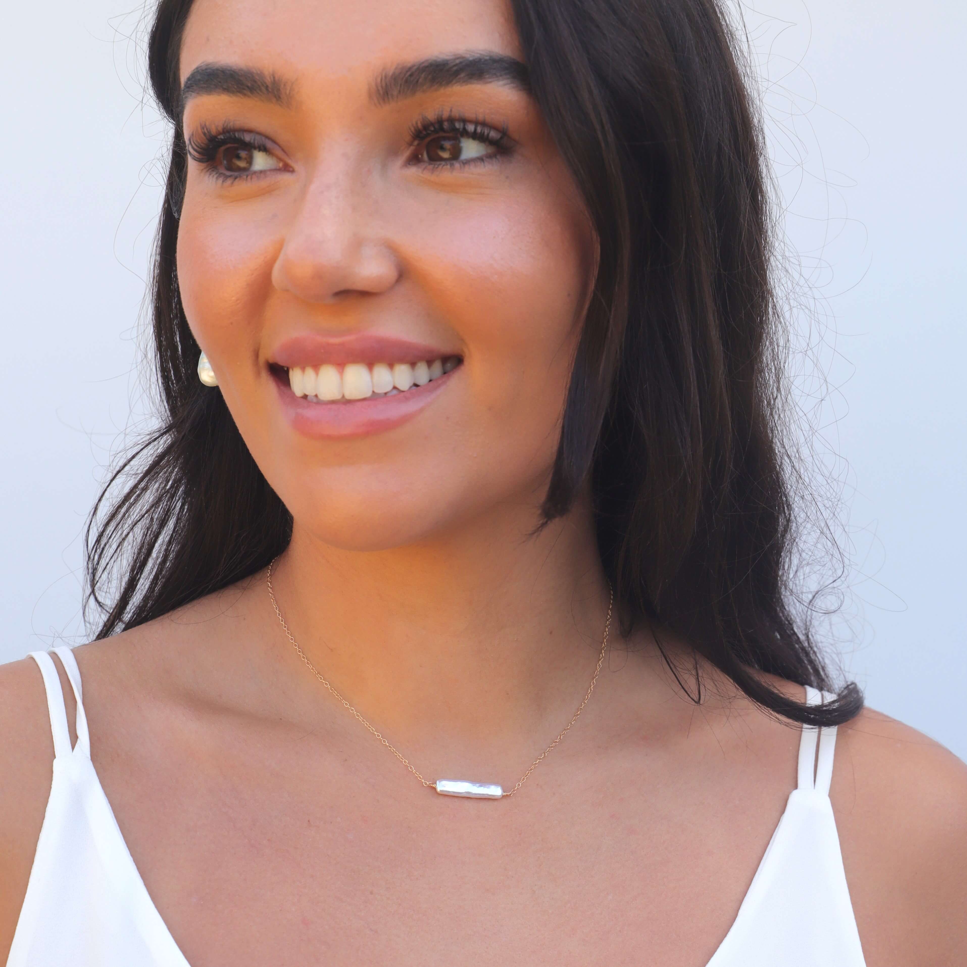Smiling model wearing white top and pearl bar necklace