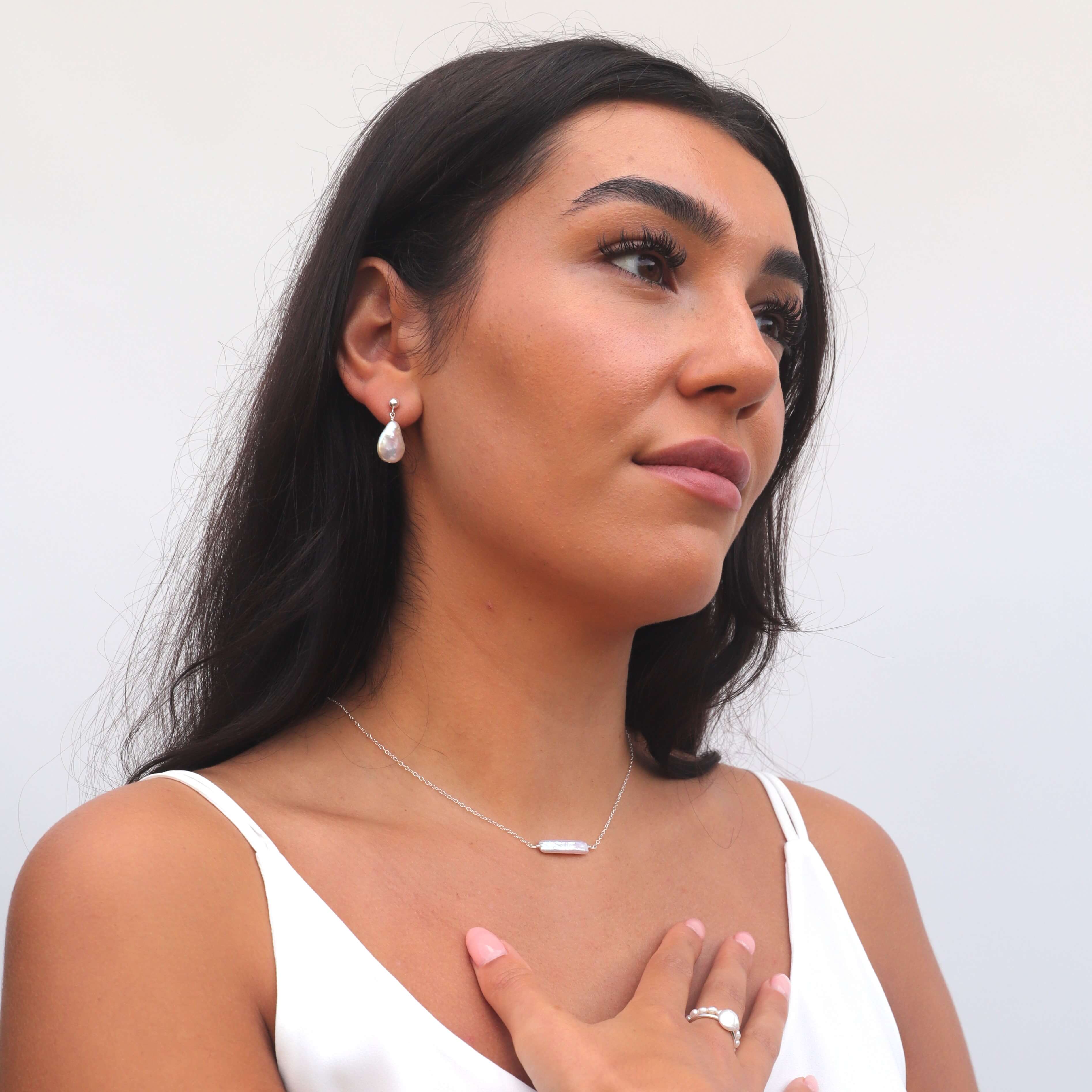 Model wearing white top rectangular pearl necklace and baroque pearl earrings