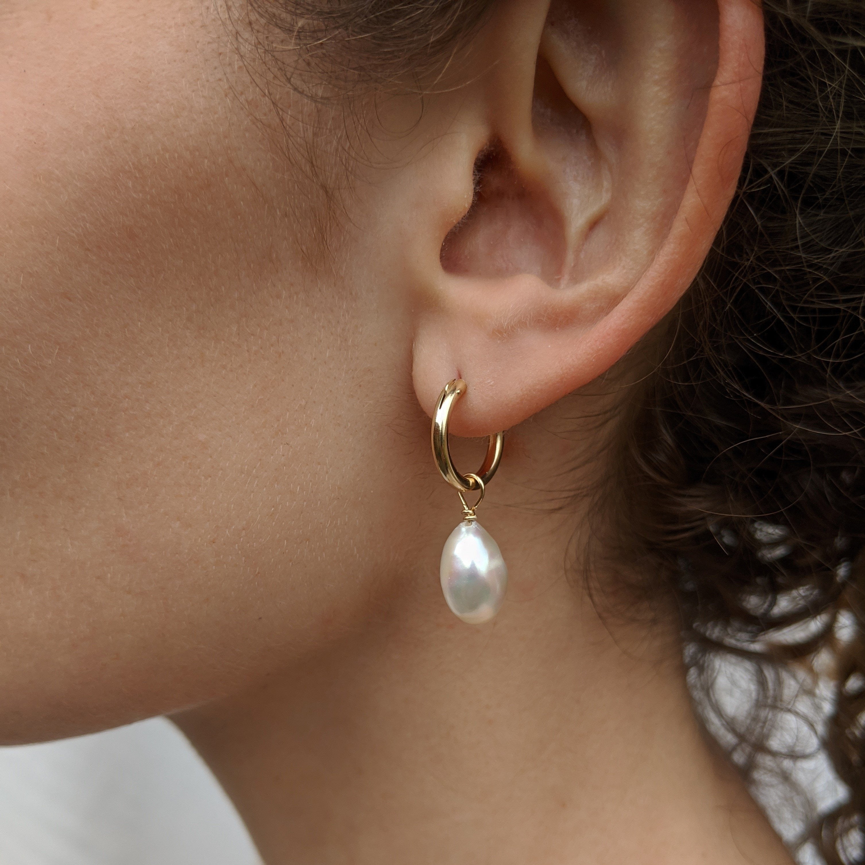 Close up of ear with a gold hoop earring with pearl