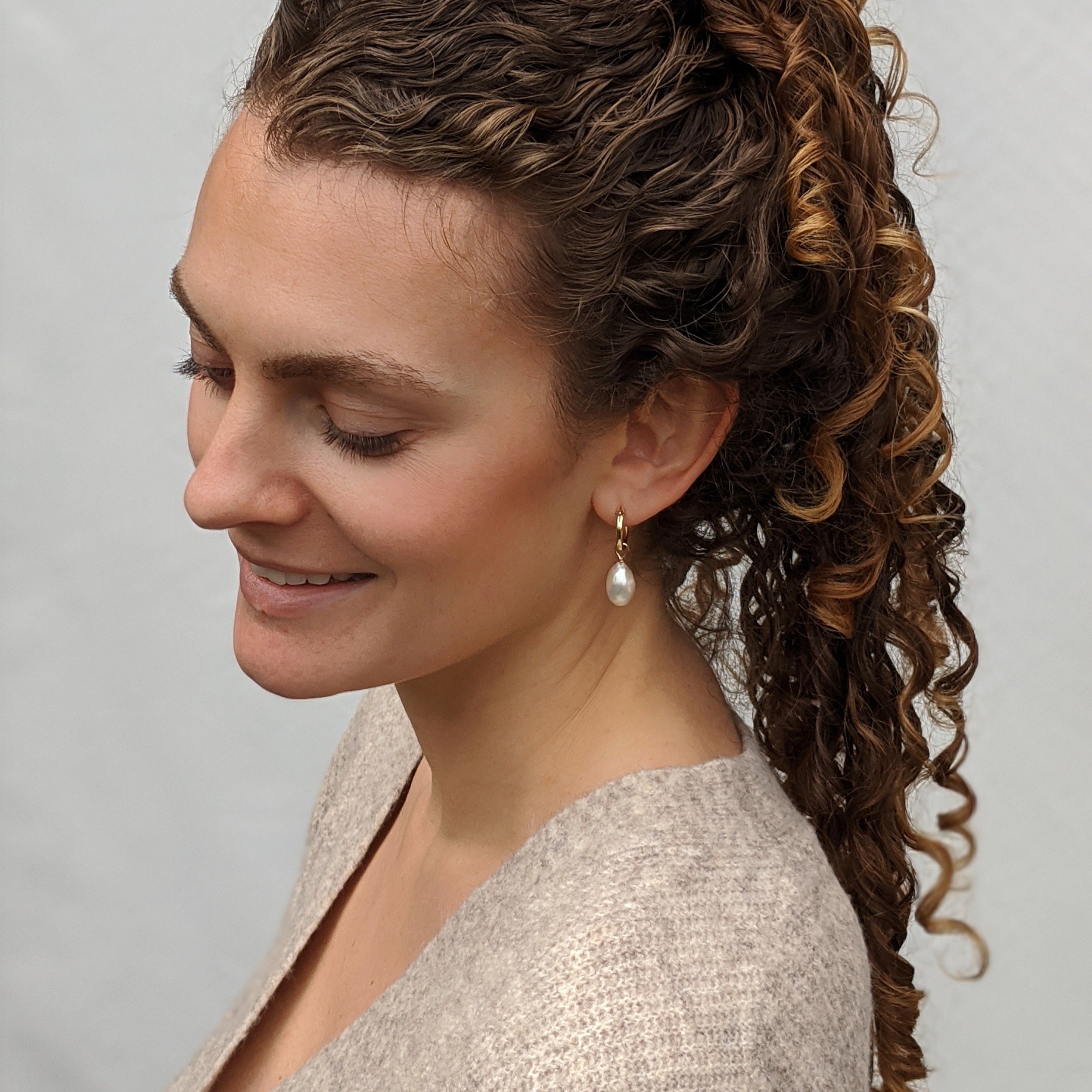 Model with curly hair wearing gold pearl hoop earrings