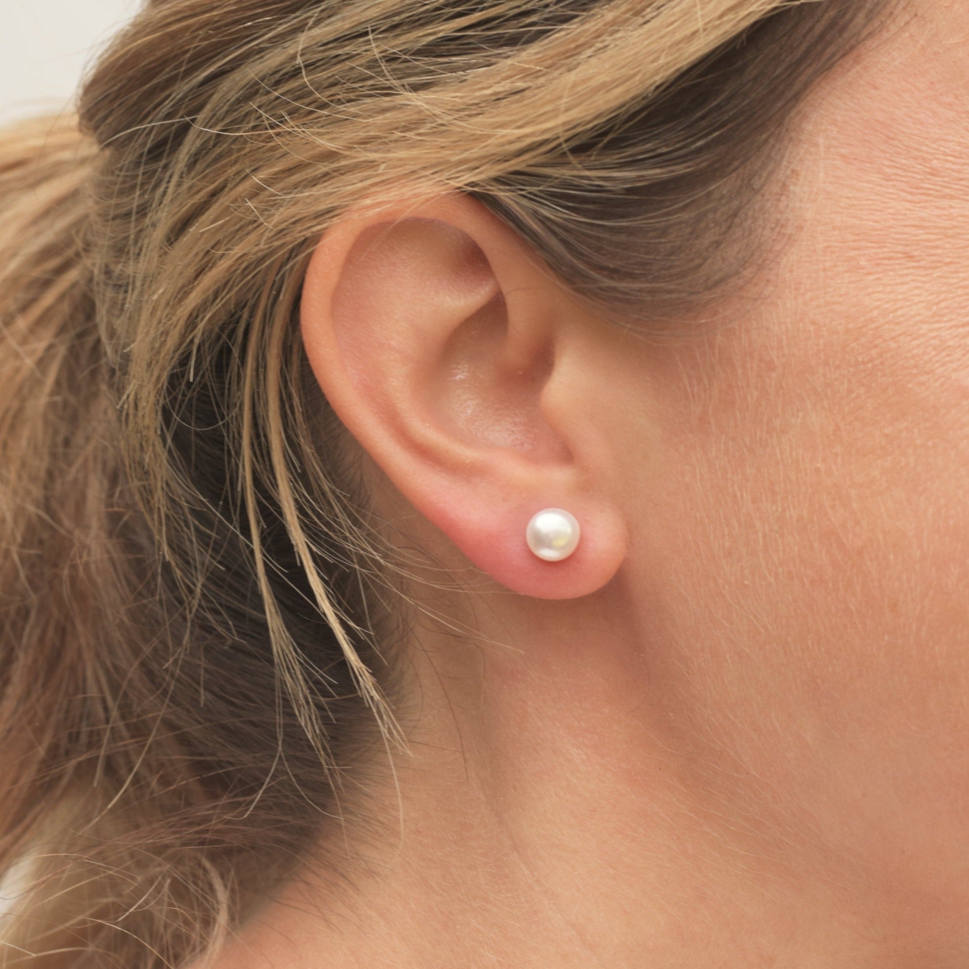 Closeup of model wearing a single white round pearl stud earring