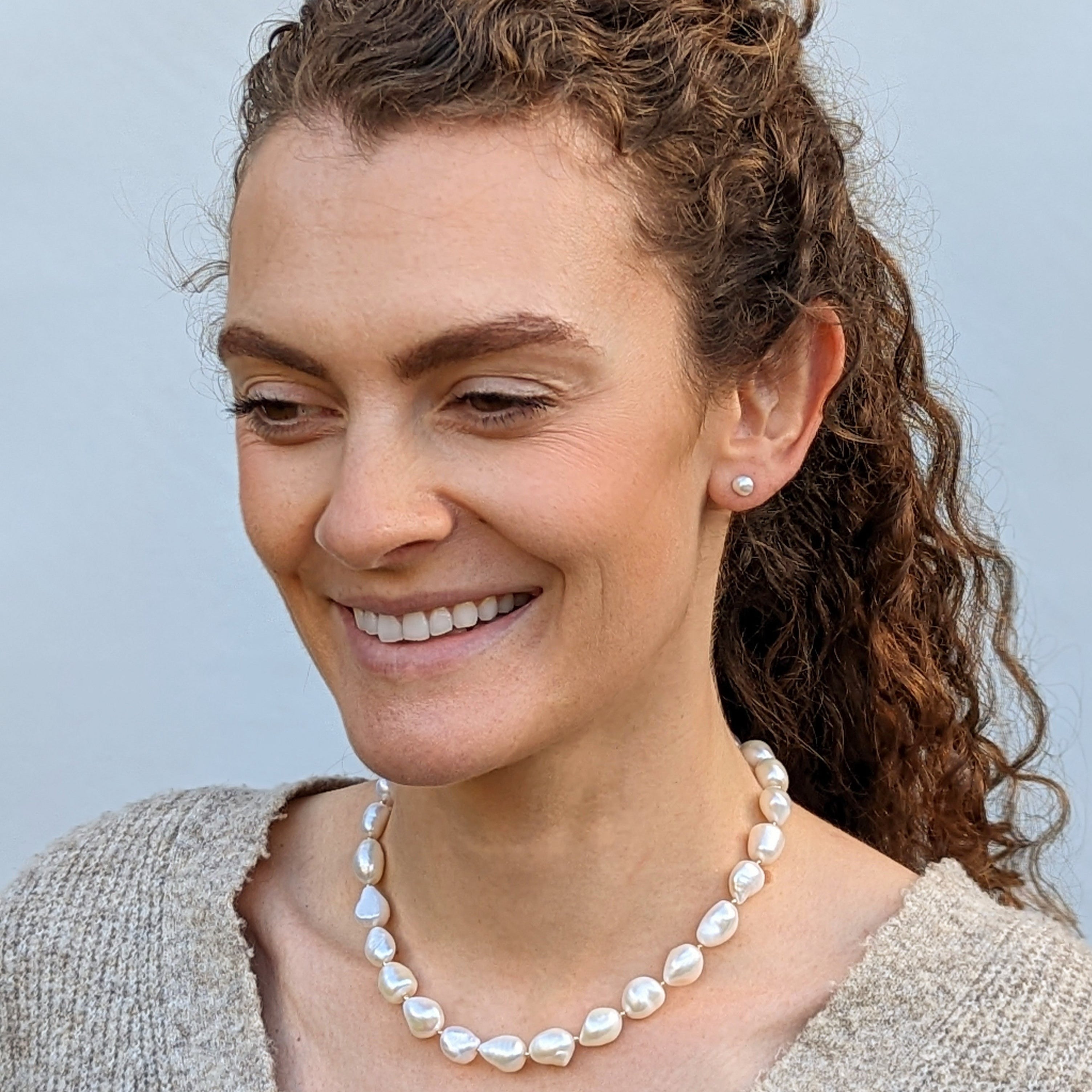 Curly hair model wearing chunky pearl necklace and pearl stud earrings