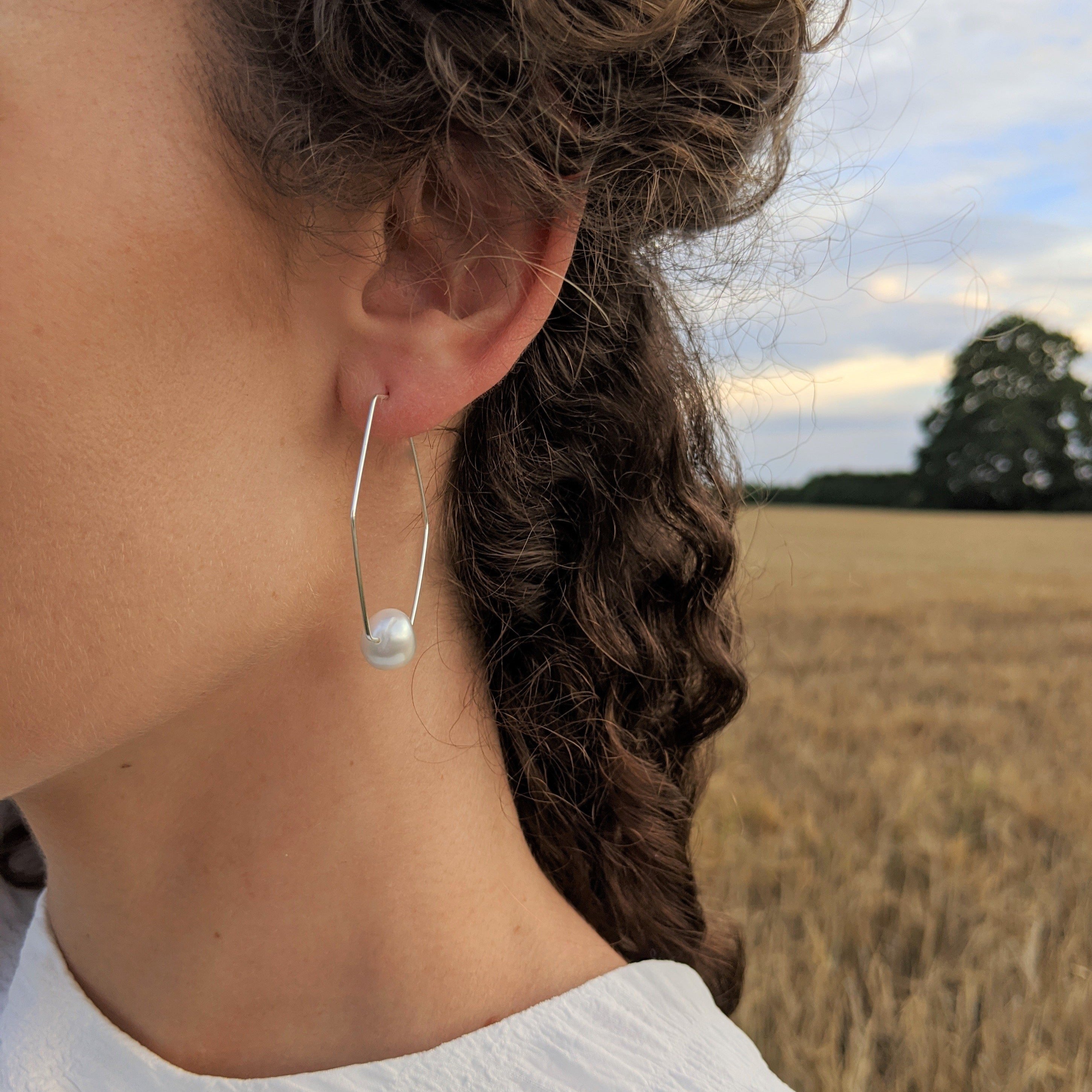 Silver geometric pearl hoop earrings on girl in a field