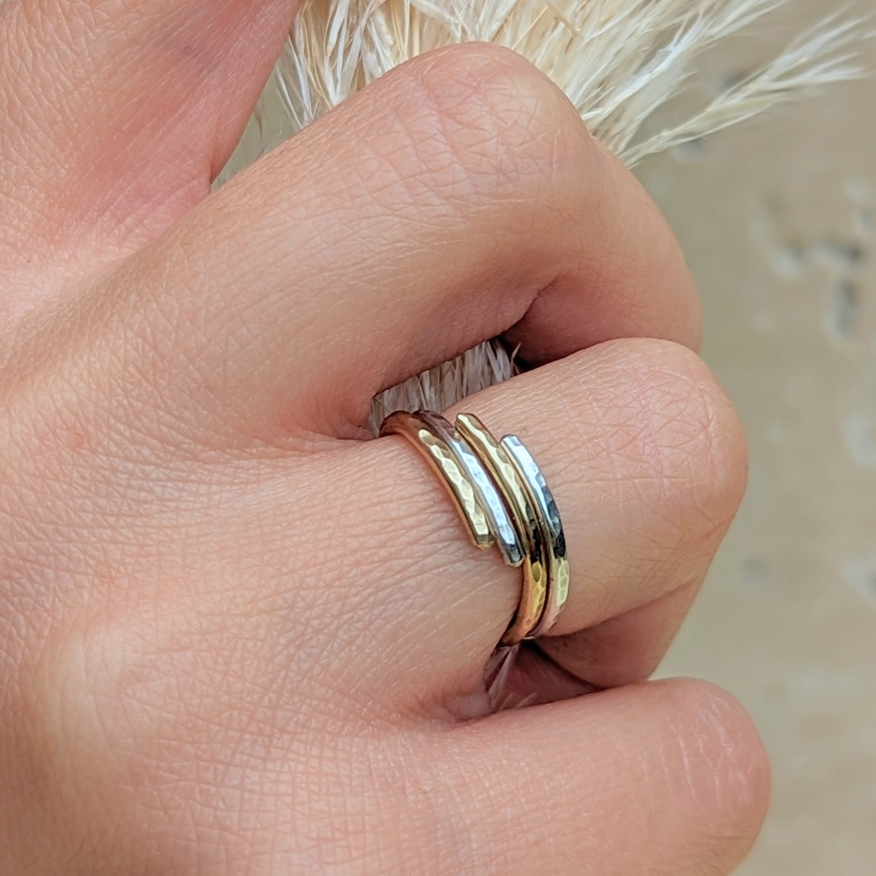 hand wearing intertwined gold and silver hammered rings 