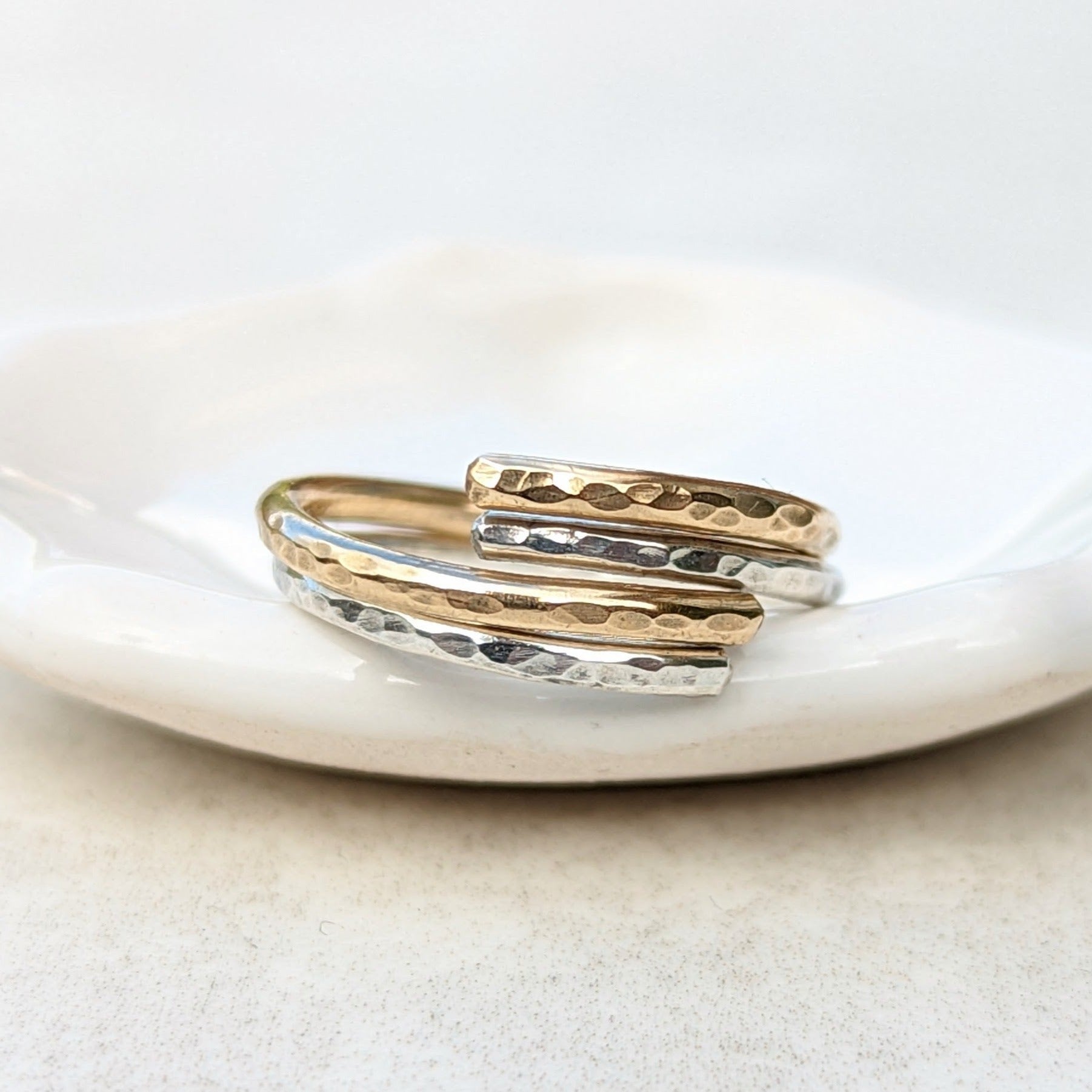 Intertwined gold and silver hammered ring stack on a trinket dish