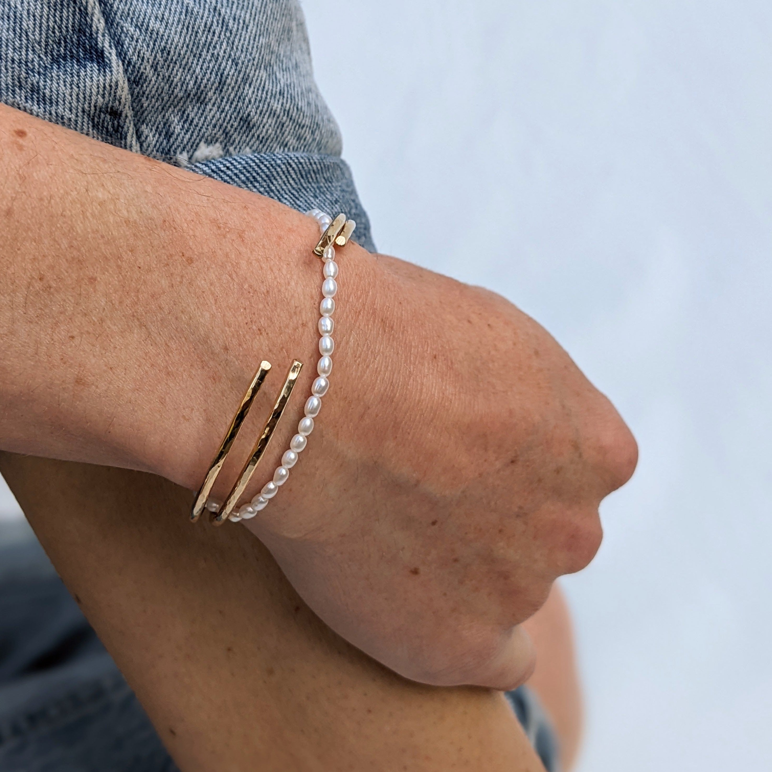 Pearl bracelet and gold cuff bracelets on model wrist