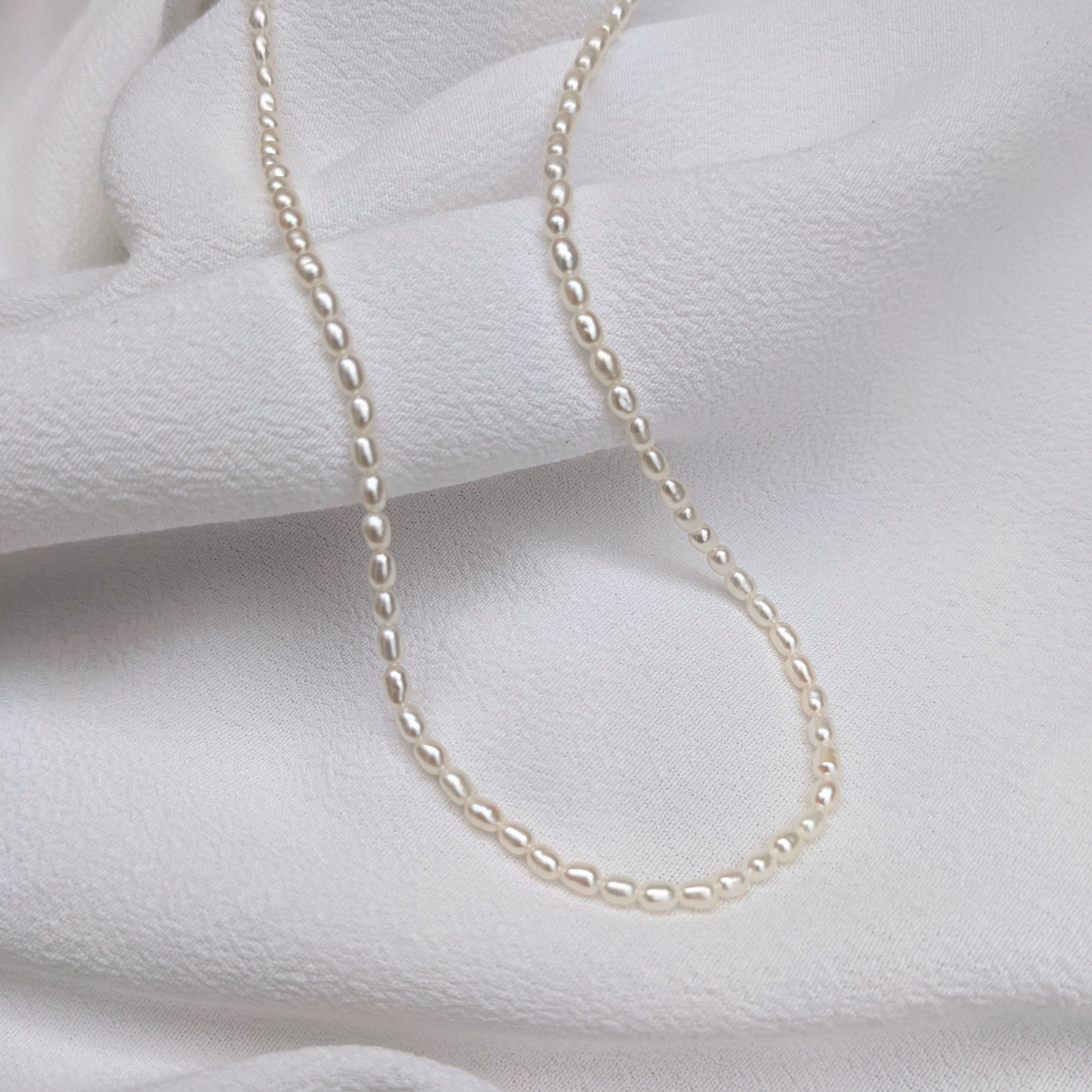 Small pearl necklace draped over white fabric