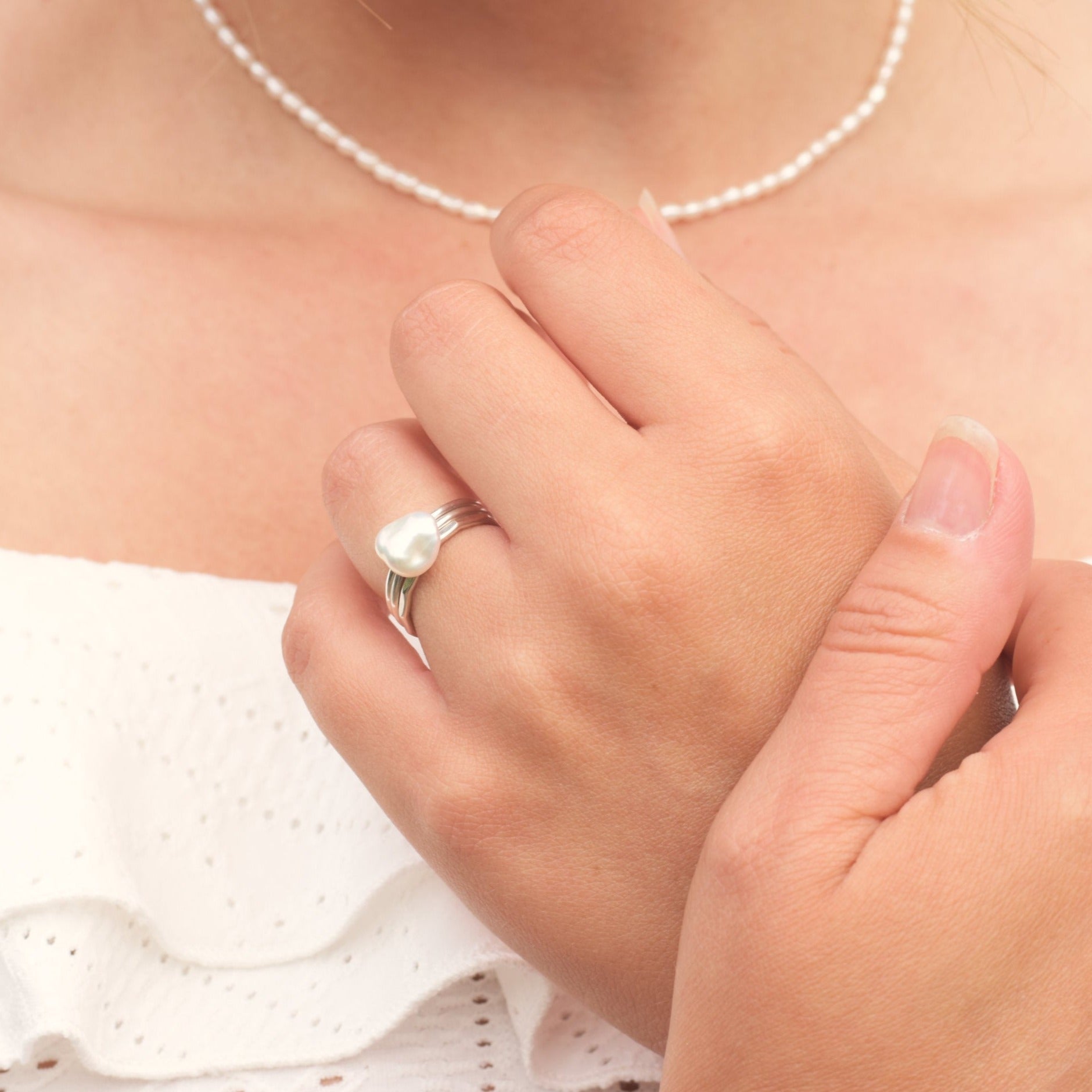 Model wearing pearl necklace and silver stacking rings