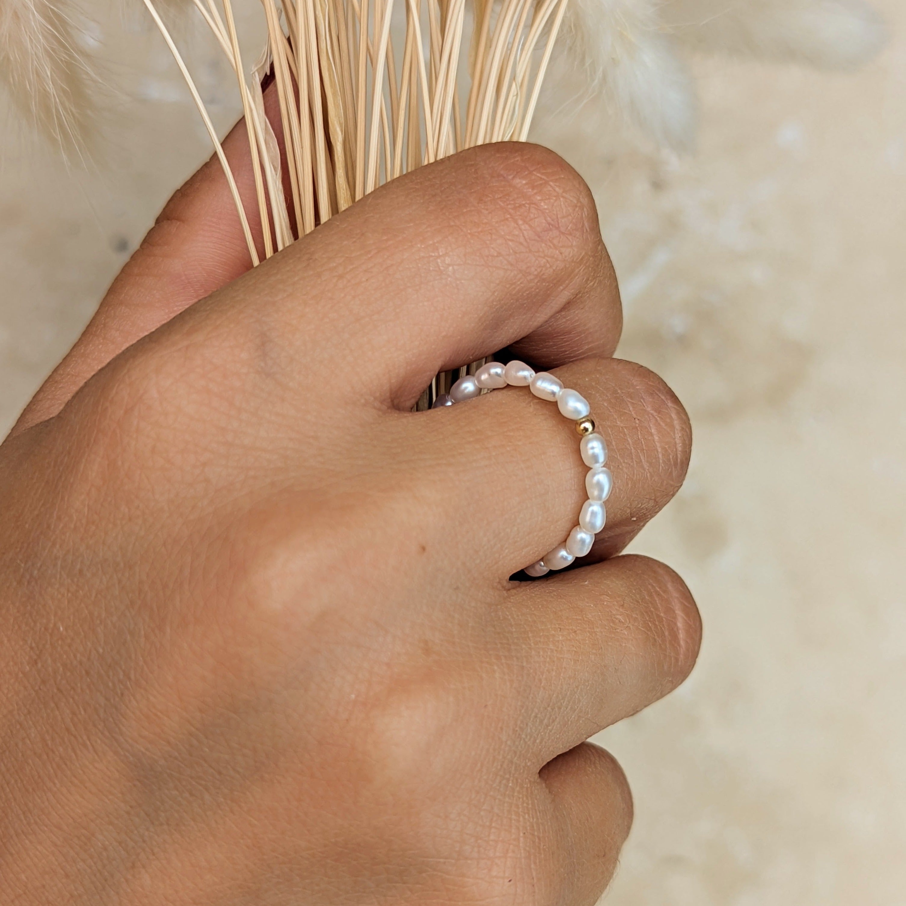 Hand holding dried grass wearing a pearl ring with small gold bead