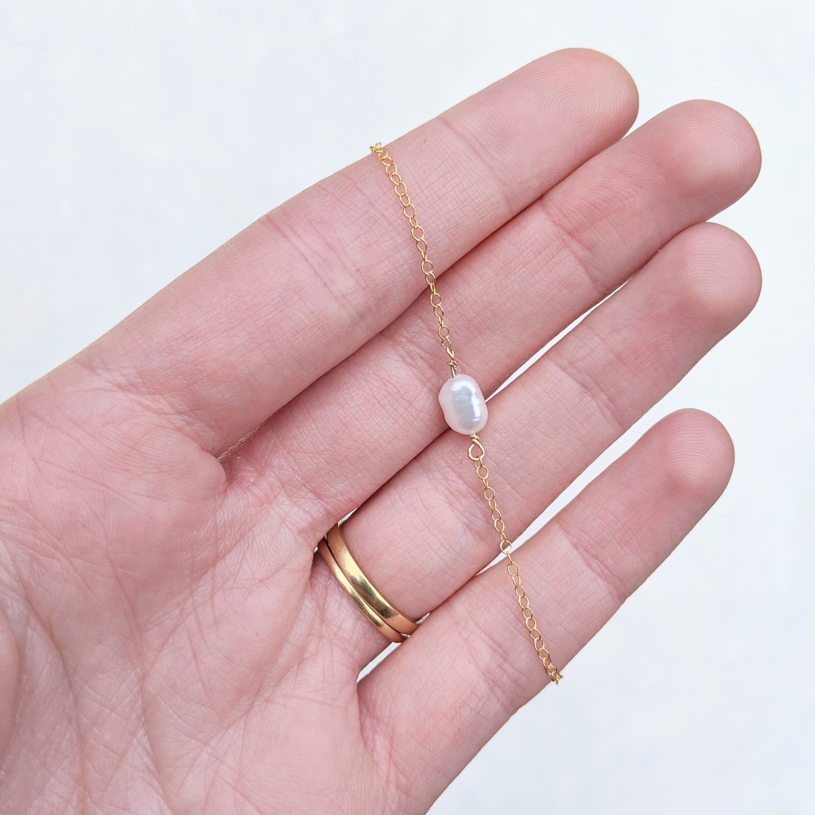 Single small white pearl on gold chain necklace in hand