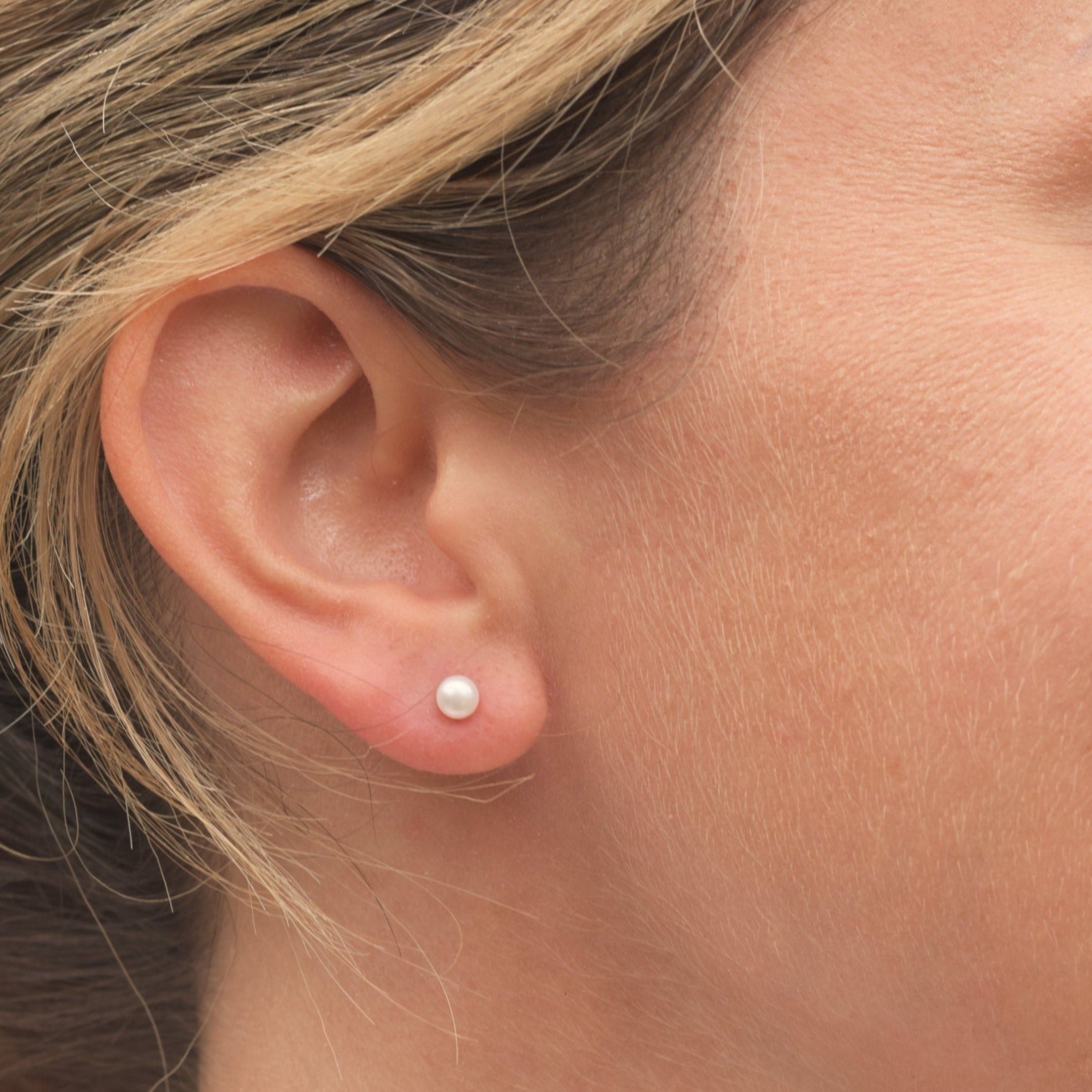 Closeup of model wearing a small white round pearl stud  earring