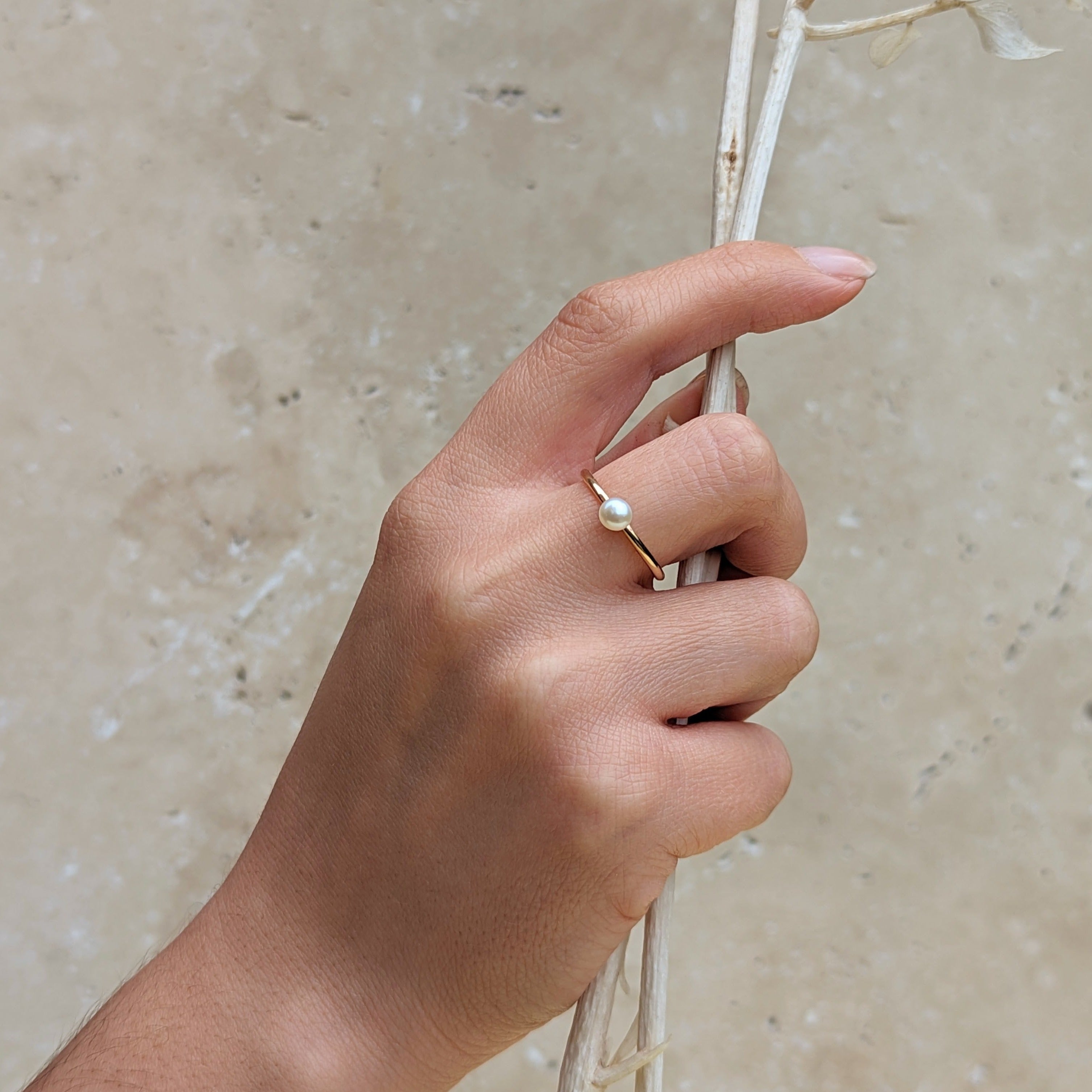 Hand holding a dried branch wearing a gold ring with a small round pearl