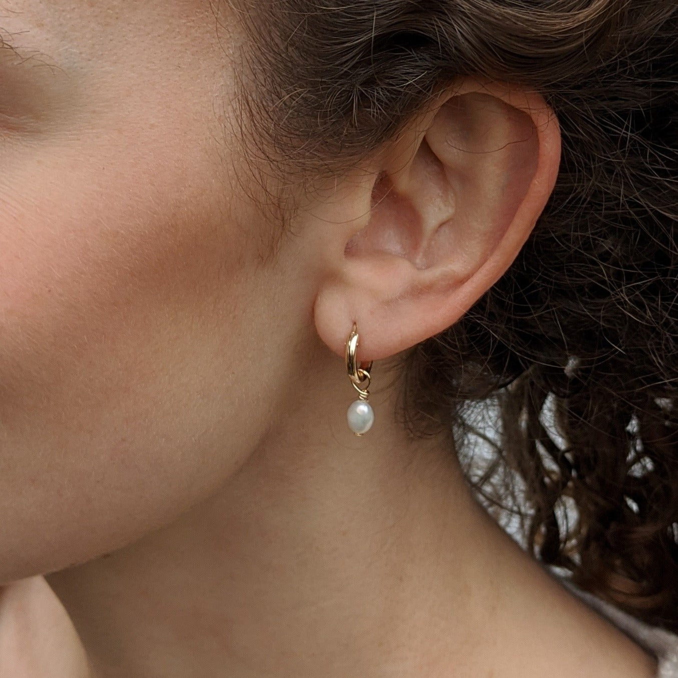 Close up of model wearing small pearl gold huggie hoop earrings