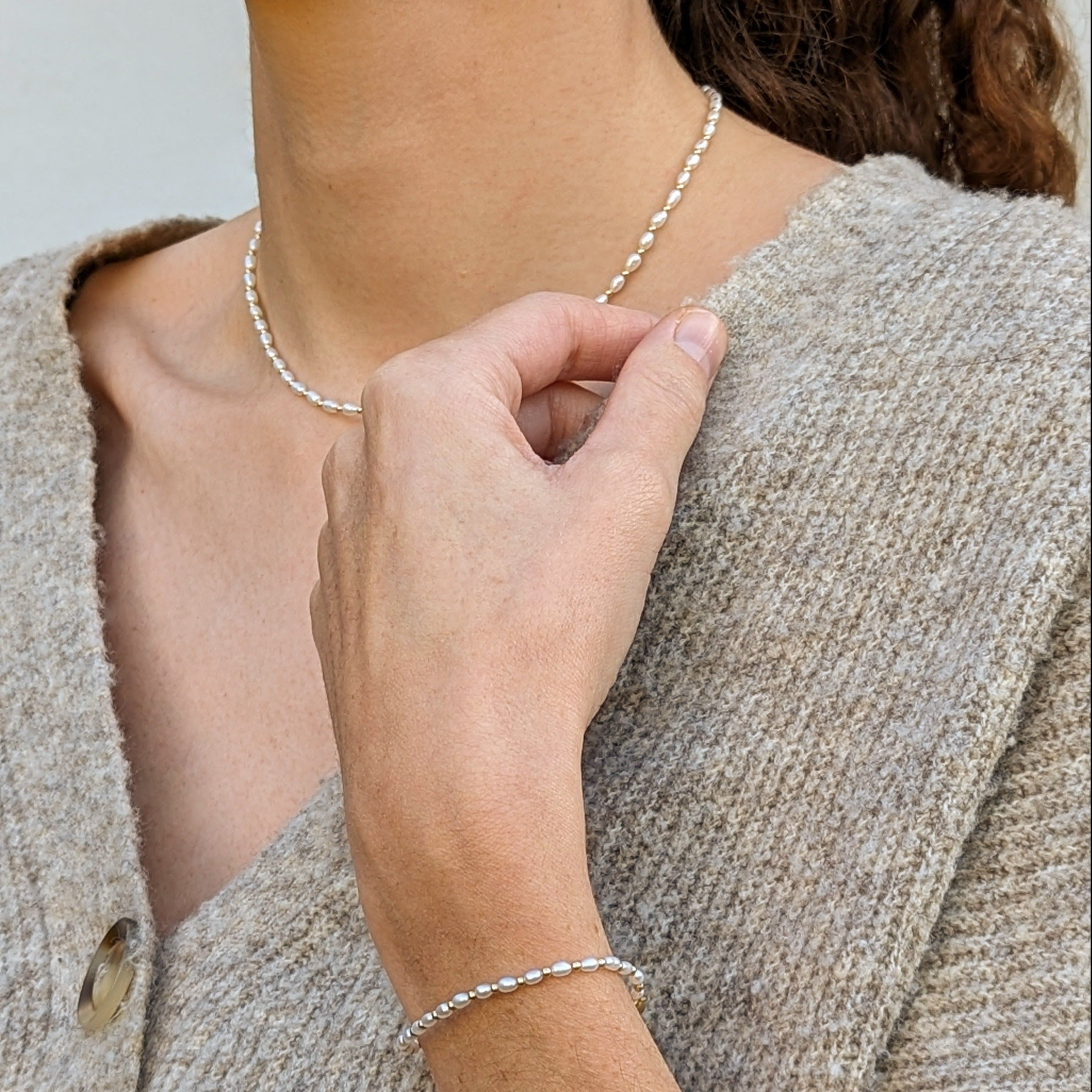 Model wearing a brown sweater and pearl and gold bead bracelet and necklace