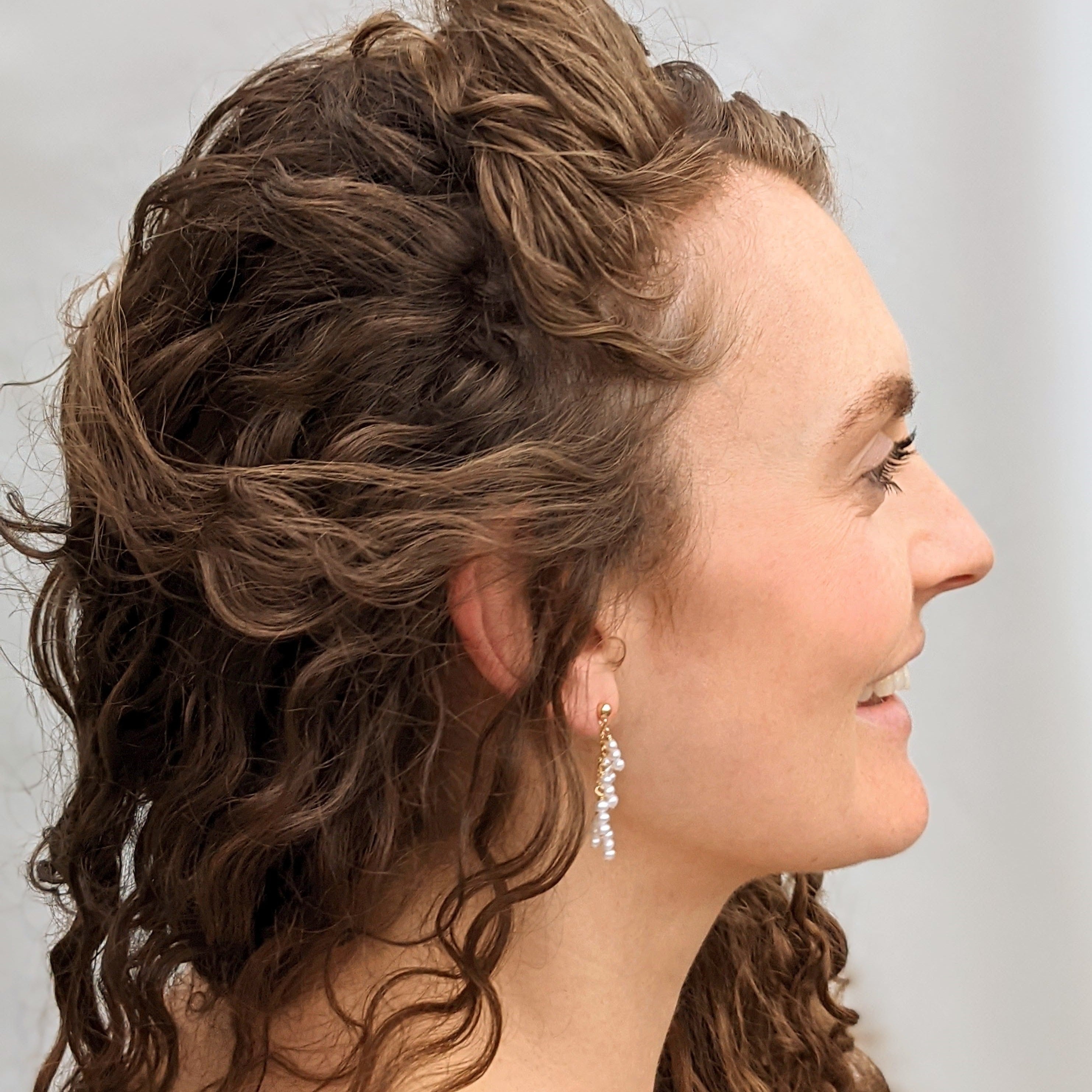 Model with curly brown hair wearing pearl earrings