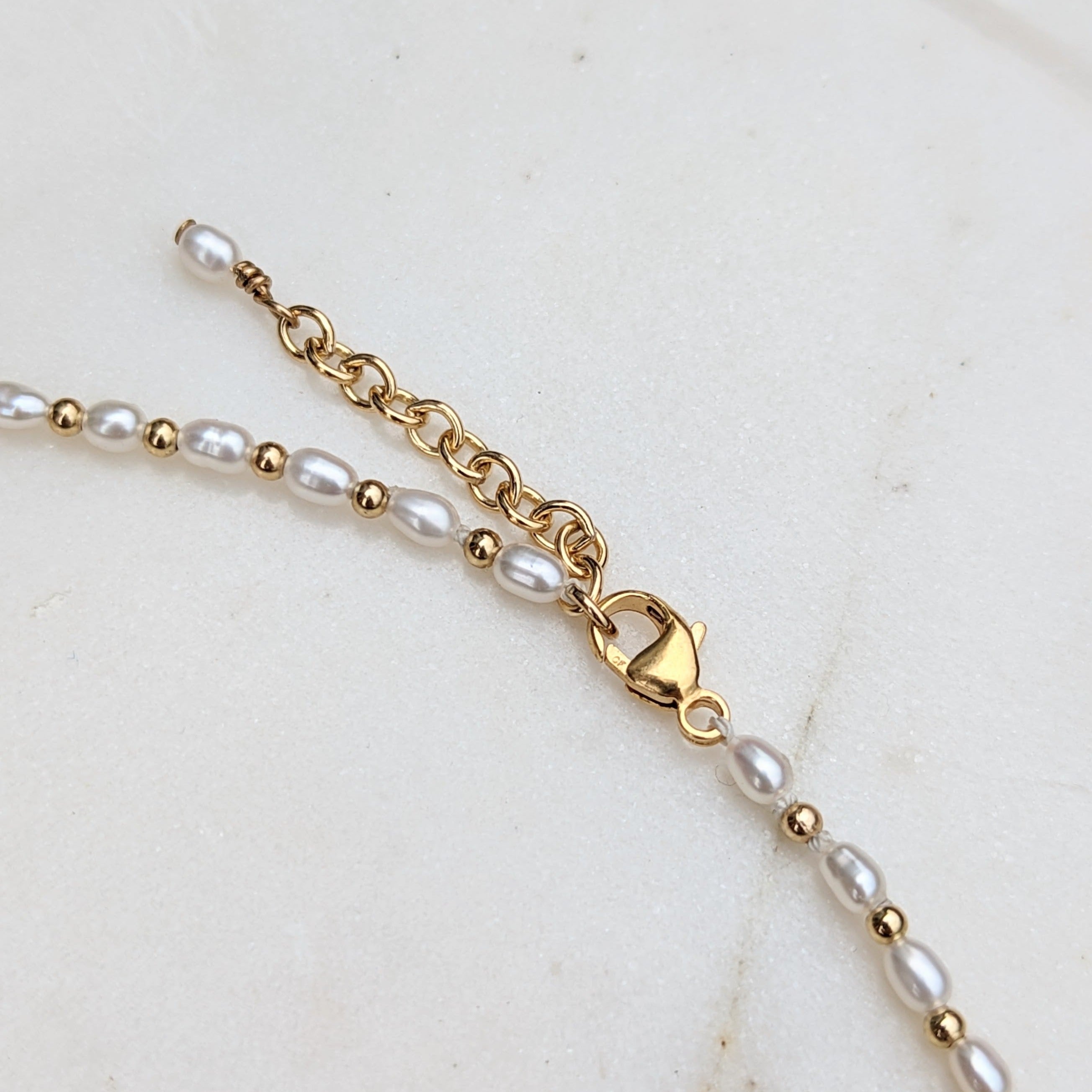 Closeup of clasp and adjustable chain on tiny pearl and gold bead necklace