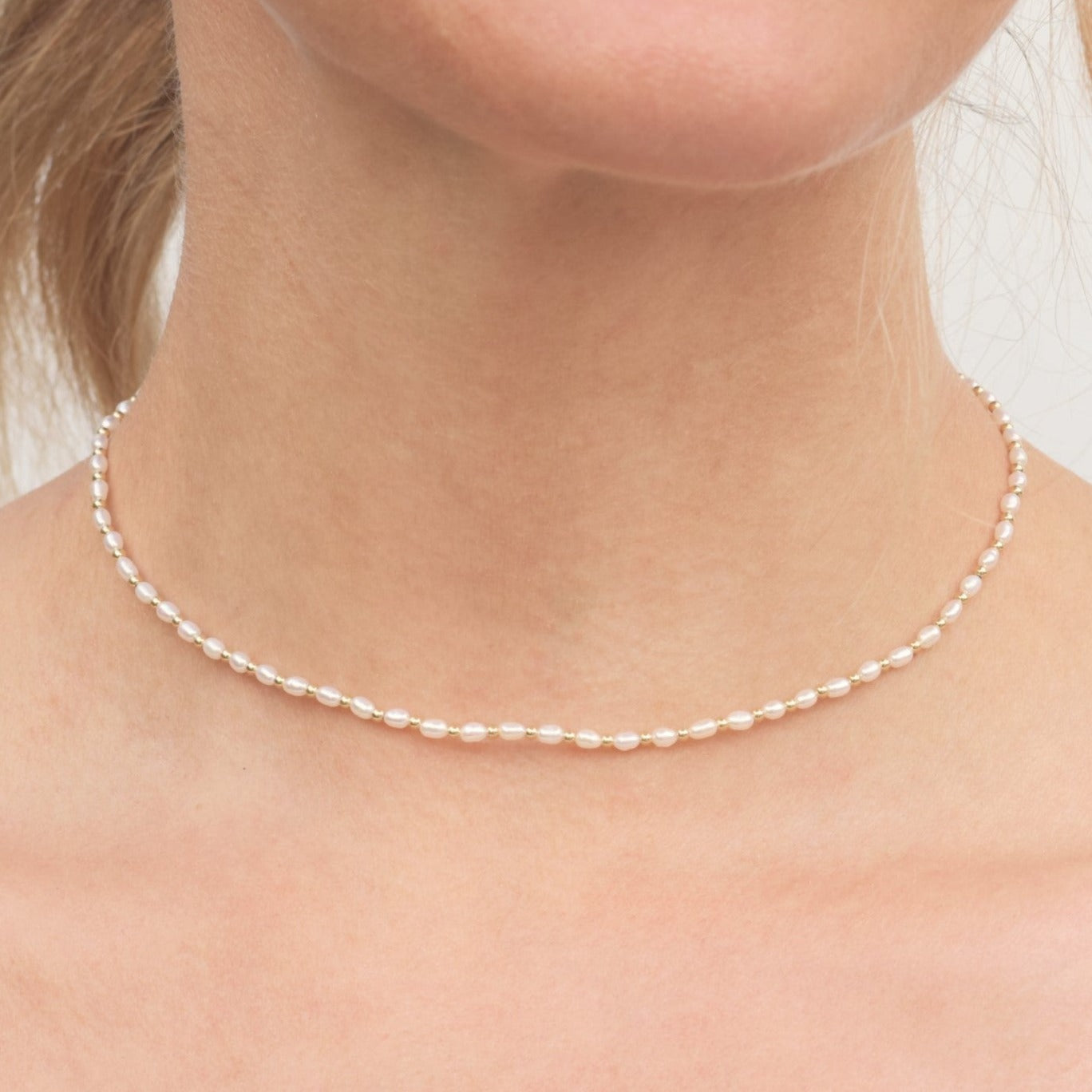 Closeup of women's neck wearing tiny pearl and bead choker necklace