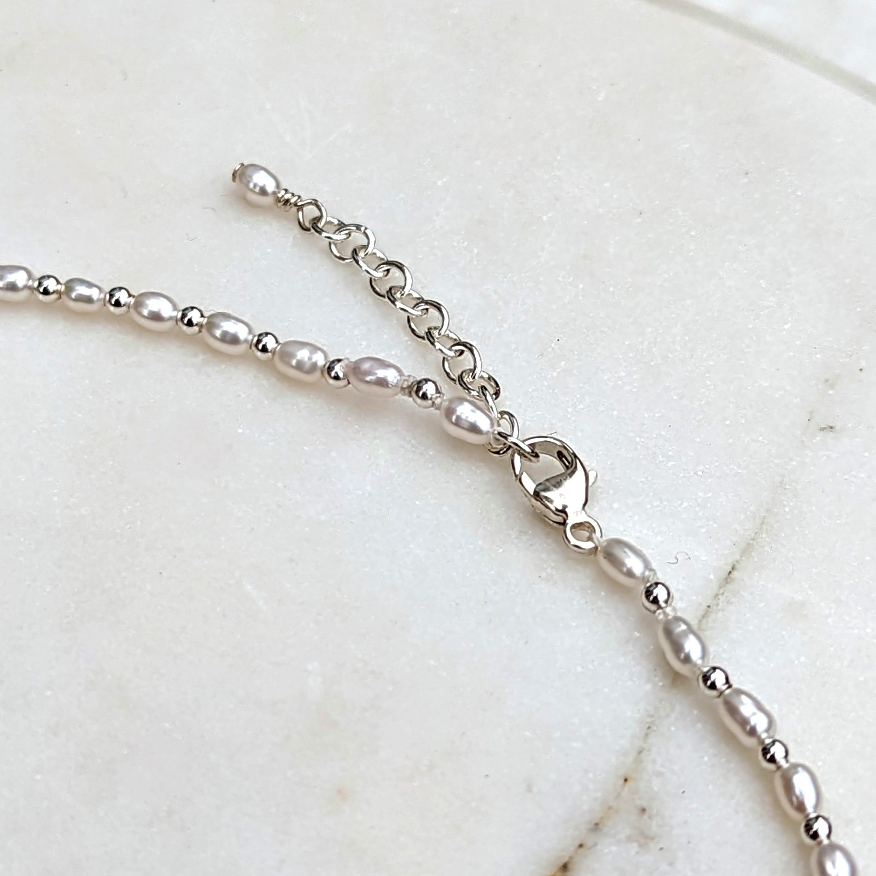 Closeup of silver clasp and chain of tiny pearl and silver bead necklace